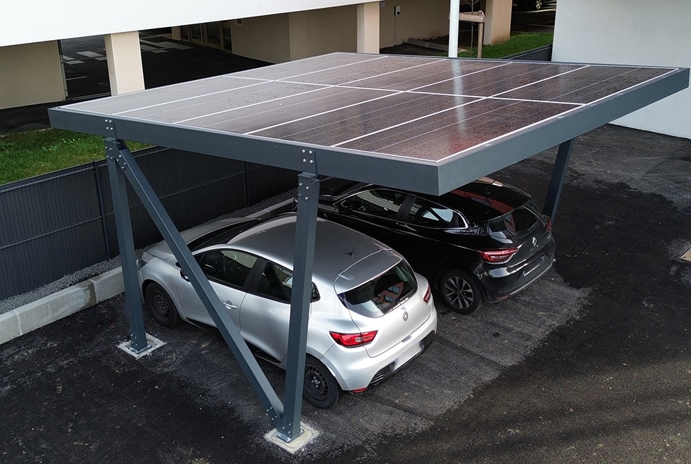 Carport solaire en aluminium anthracite abritant deux voitures sur un parking au pied d'un immeuble