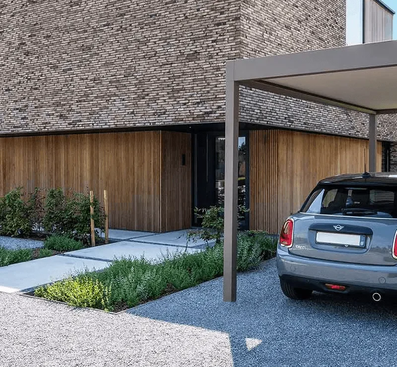 Carport autoportant en aluminium abritant une petite voiture dans l'allée en gravier d'une maison contemporaine