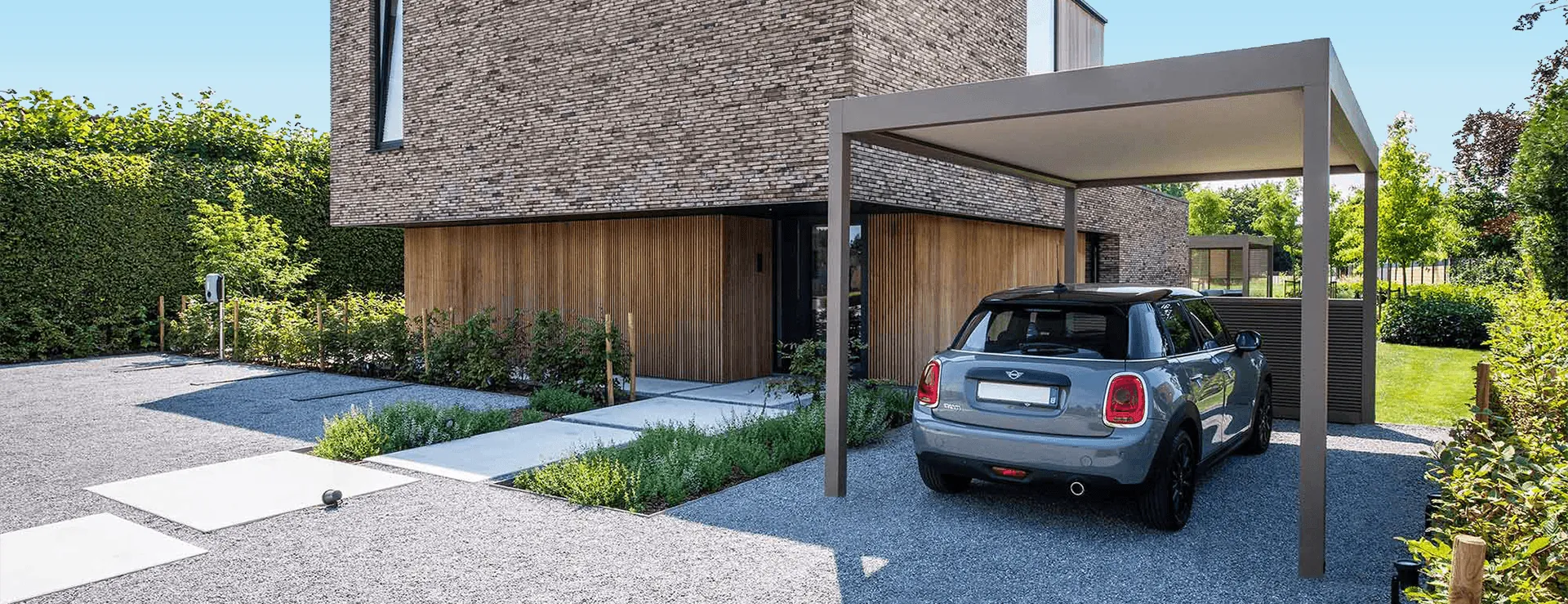 Carport autoportant en aluminium abritant une petite voiture dans l'allée en gravier d'une maison contemporaine