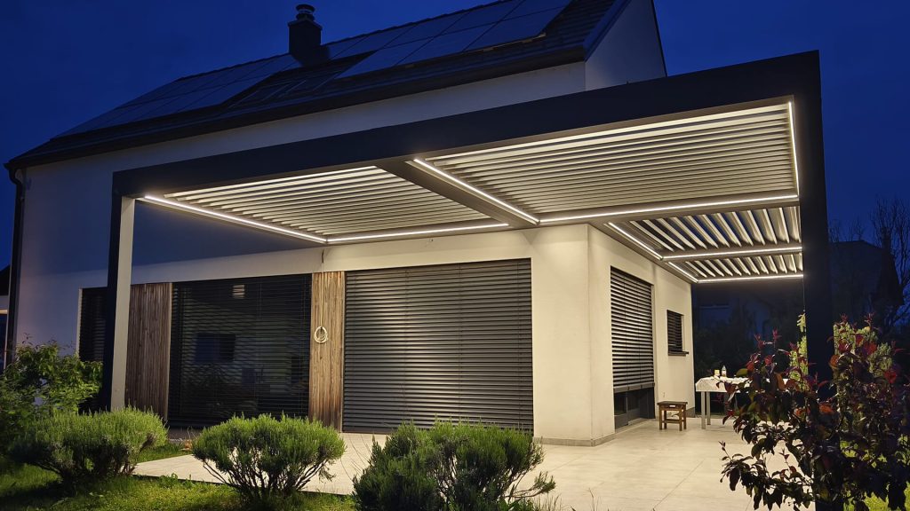 Une grande terrasse qui vit aussi le soir Grande pergola adossée à une maison, éclairée de nuit par des bandes LED le long des lames