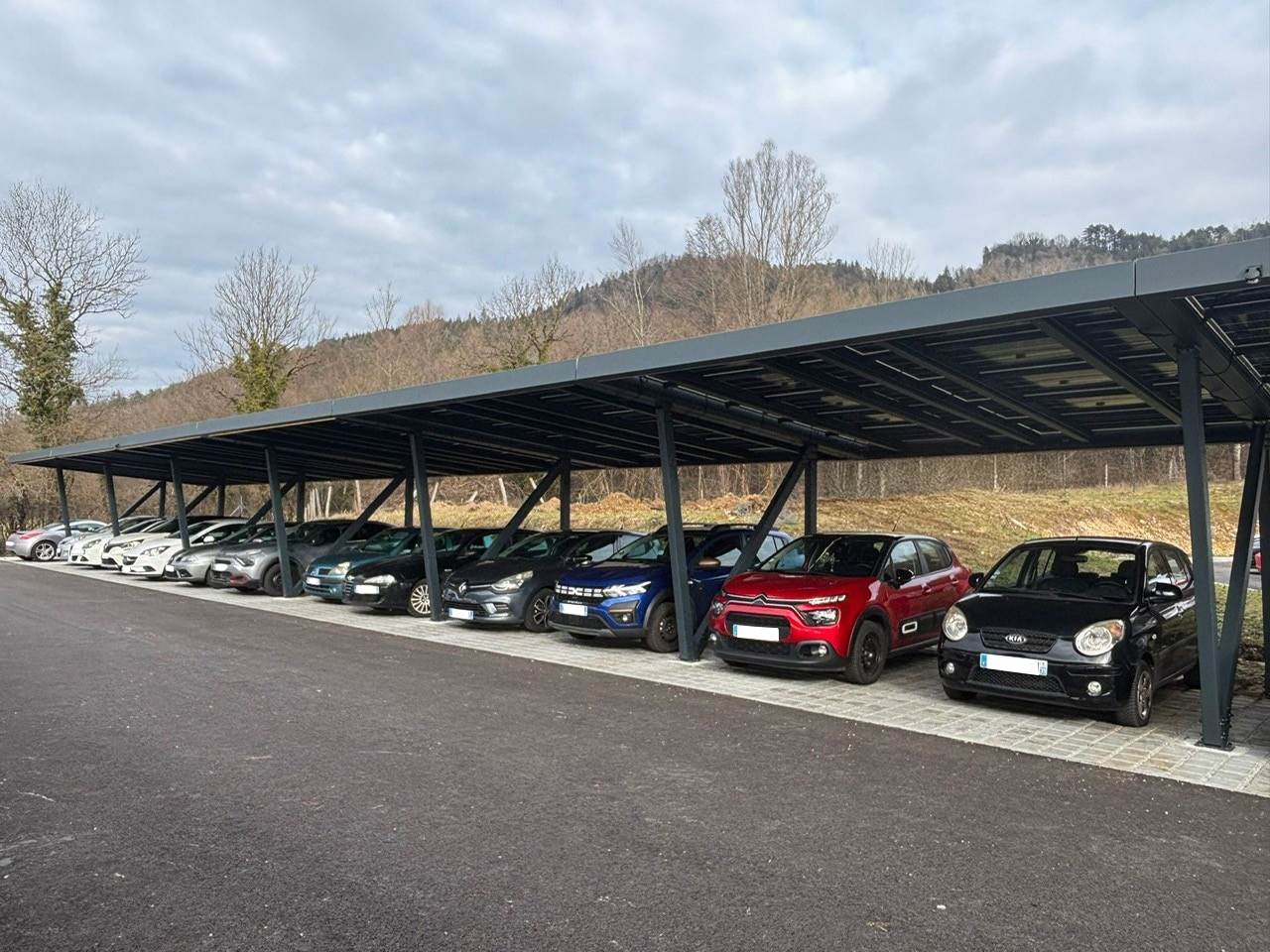 Longue ombrière solaire en aluminium anthracite couvrant une rangée de voitures sur un parking