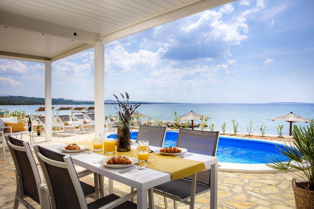 Une terrasse adossée face à la mer Pergola blanche adossée abritant une table de petit-déjeuner, face à une piscine et à la mer