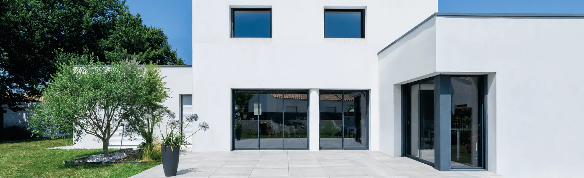 Maison contemporaine aux grandes baies vitrées et sa terrasse dallée sans protection, avant l'installation d'une pergola