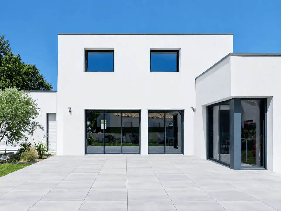 Façade blanche d'une maison contemporaine et sa terrasse dallée sans couverture, avant la pose d'une pergola