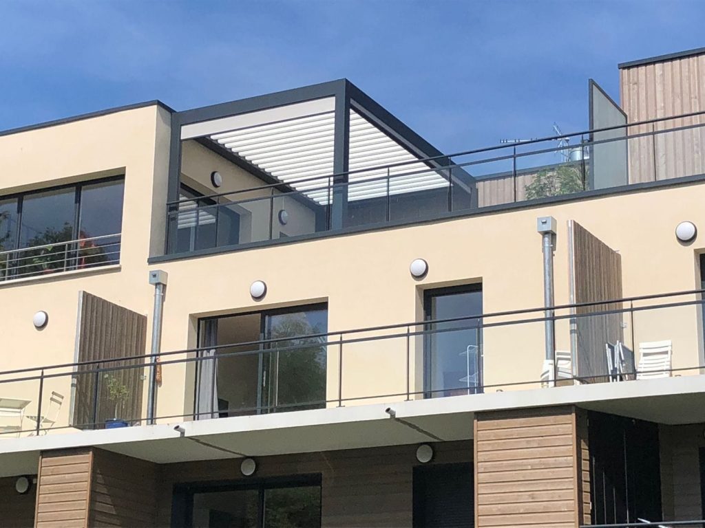 Une terrasse en attique couverte Pergola bioclimatique à structure anthracite et lames blanches sur la terrasse en attique d'un immeuble résidentiel