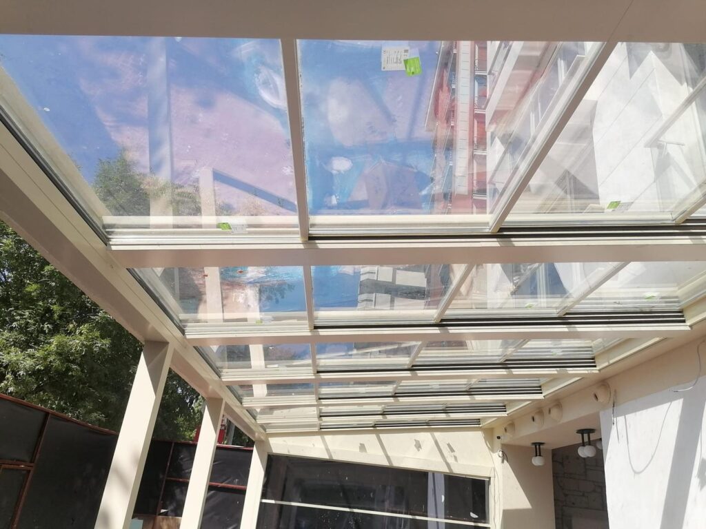 Une pergola vitrée en fin de pose Intérieur d'une pergola vitrée à toit en verre coulissant et profilés beiges, en cours de finition