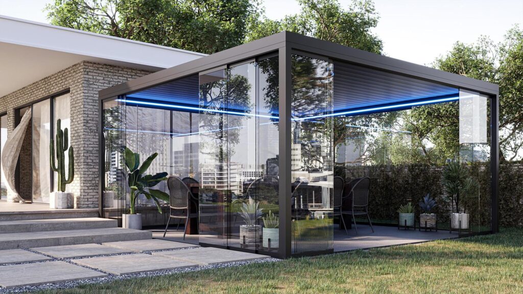 Une pergola vitrée dans le prolongement de la maison Pergola en aluminium à toit à lames, fermée par des parois vitrées coulissantes et éclairée par des LED, devant une maison