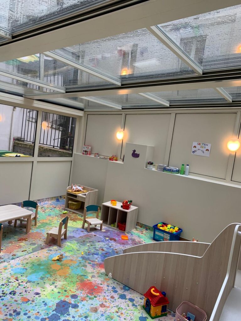 Espace de jeux pour enfants sous une pergola vitrée Pergola à toit vitré aménagée en espace de jeux, avec mobilier pour enfants et toboggan
