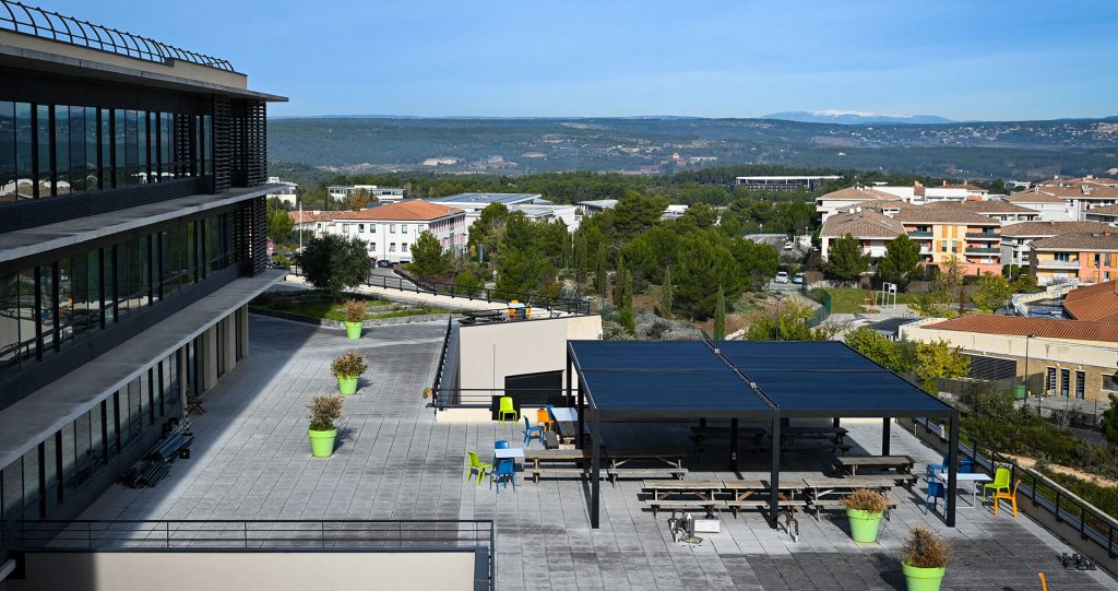 Des pergolas sur le toit d'un bâtiment professionnel Pergolas bioclimatiques noires sur le vaste toit-terrasse d'un bâtiment, avec des tables et une vue dégagée sur la campagne