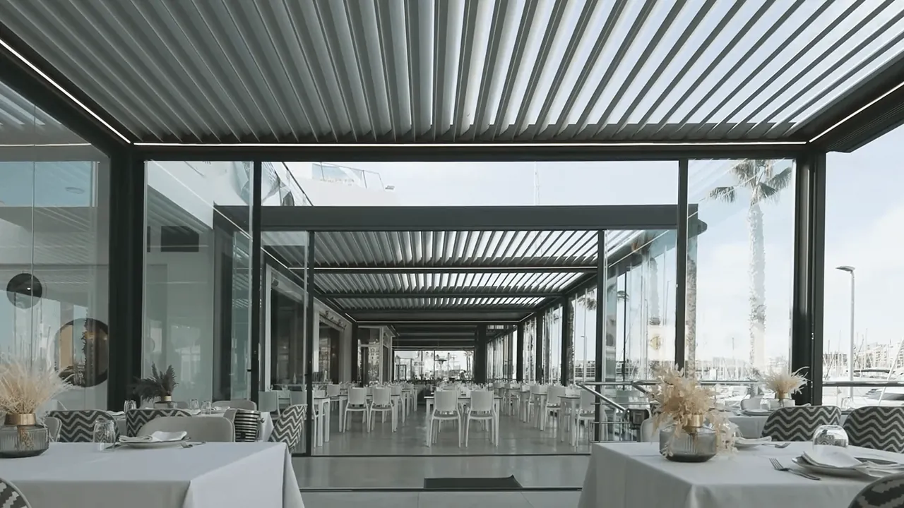 Terrasse de restaurant couverte par des pergolas bioclimatiques et fermée par des rideaux de verre, au bord d'un port