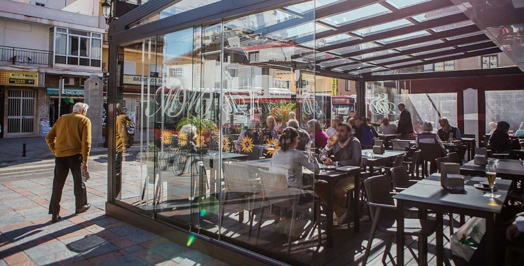 Une terrasse de restaurant utilisable plus longtemps Terrasse de restaurant sous une toiture vitrée, fermée par des rideaux de verre, avec des clients attablés