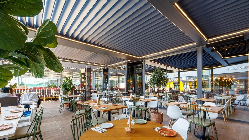 Une grande terrasse de restaurant couverte Grande pergola bioclimatique aux lames fermées et à l'éclairage LED intégré, couvrant la terrasse d'un restaurant
