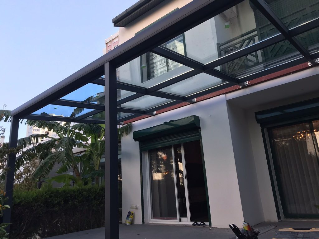 Un toit vitré contre la façade Toit vitré à structure aluminium anthracite adossé à la façade blanche d'une maison, au-dessus d'une terrasse