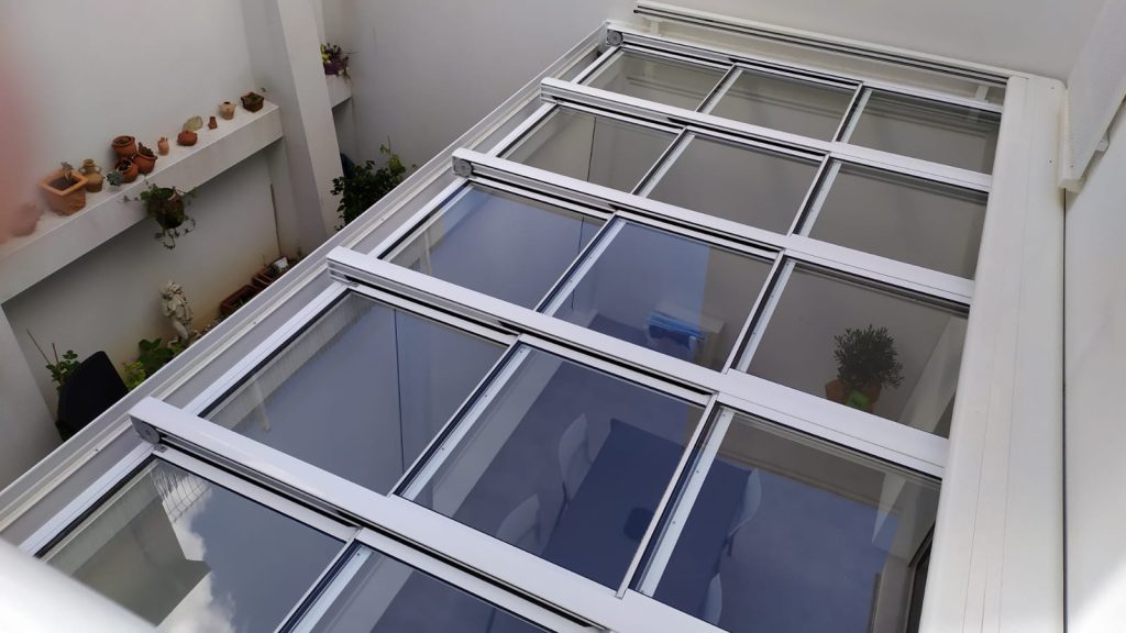 Un patio lumineux et abrité Toit vitré coulissant à profilés blancs couvrant un patio entre deux murs, vu d'en haut