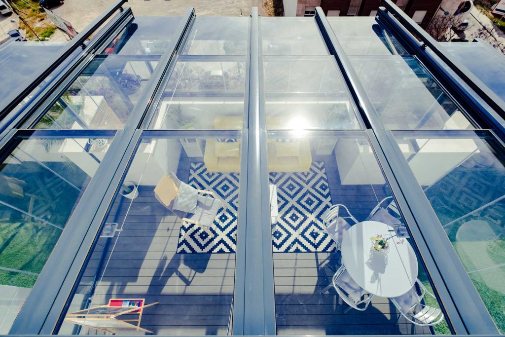 Une terrasse privée sous un toit de verre Vue de dessus d'un toit vitré coulissant laissant voir une terrasse meublée avec un tapis graphique