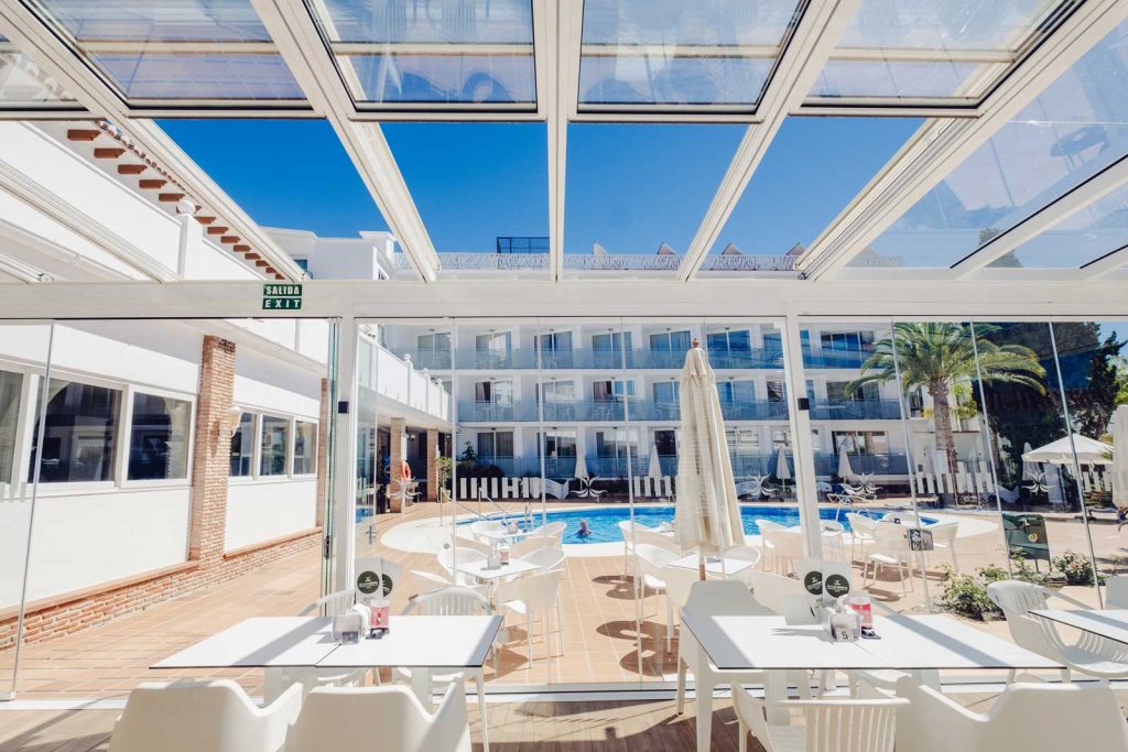Une terrasse d'hôtel qui s'ouvre sur le ciel Toit vitré rétractable blanc ouvert sur le ciel au-dessus d'une terrasse de restaurant, face à la piscine d'un hôtel