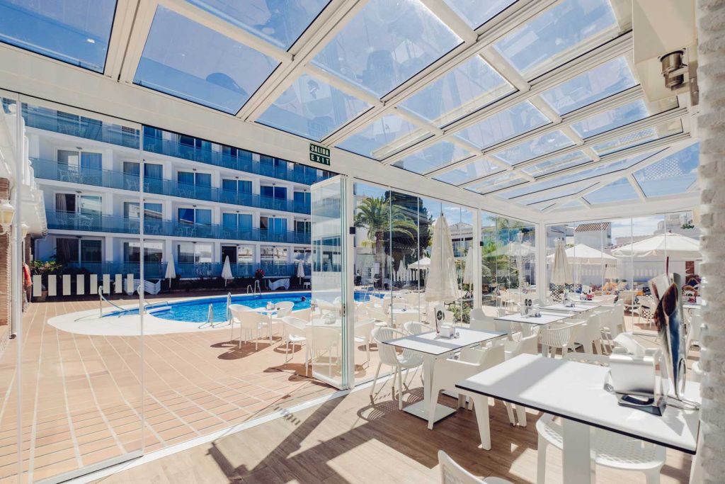 Un restaurant d'hôtel sous un toit de verre Terrasse de restaurant d'hôtel couverte d'un toit vitré rétractable blanc, avec vue sur la piscine