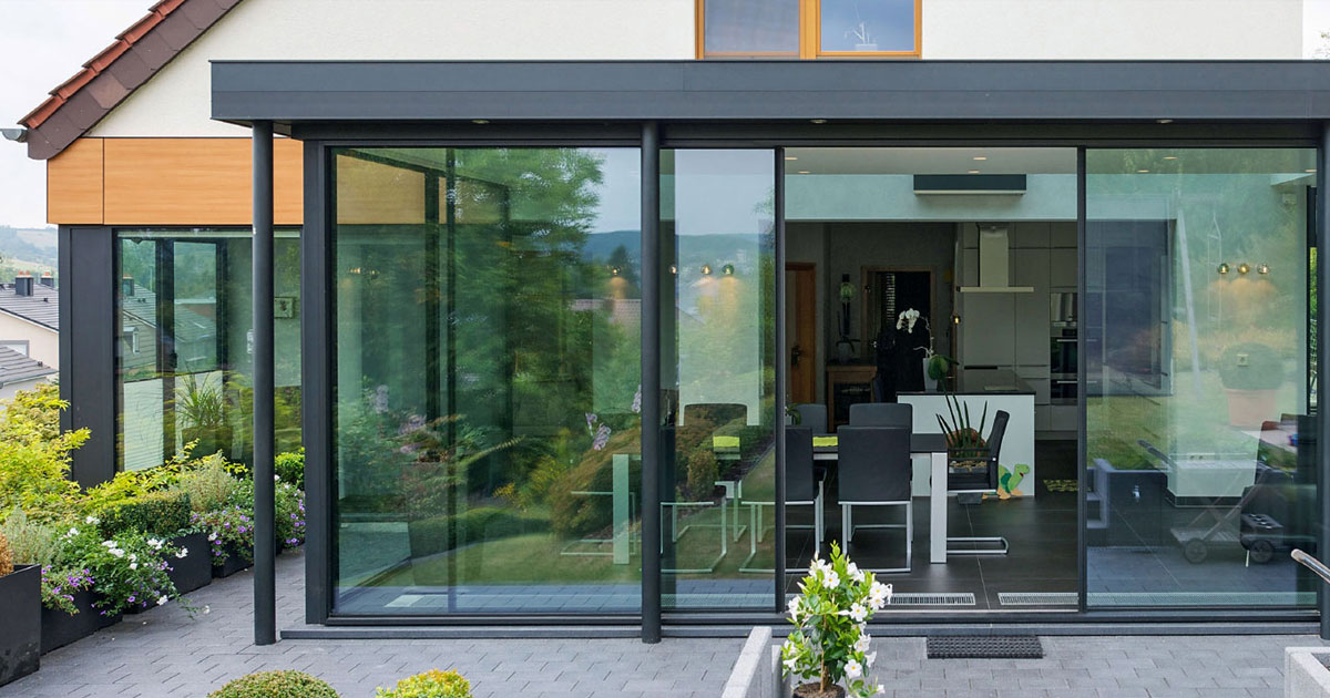 Pergola vitrée en aluminium anthracite à grandes parois vitrées coulissantes, devant une cuisine et un coin repas