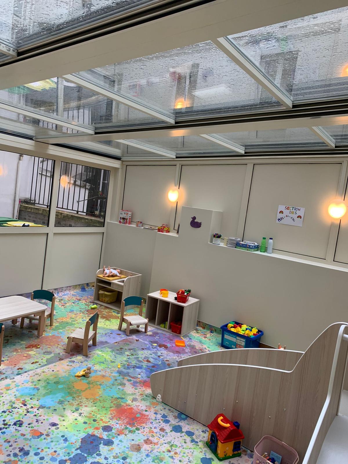 Pergola à toit vitré aménagée en espace de jeux, avec mobilier pour enfants et toboggan